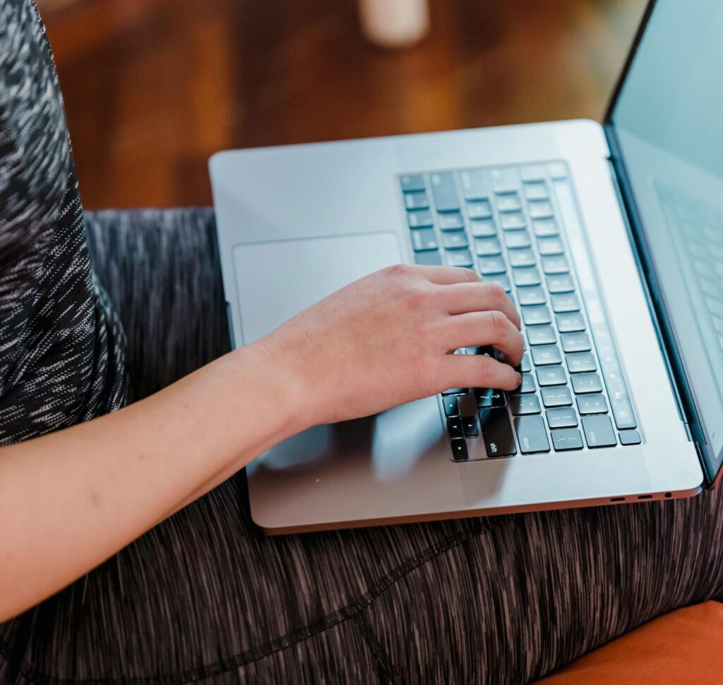A woman typing on a laptop while sitting comfortably indoors, showcasing modern technology usage.